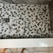 Sliced river rock mosaic shower floor in shades of charcoal and tan with a square stainless steel drain, showcasing a slip-resistant and organic design for a custom NH bathroom renovation