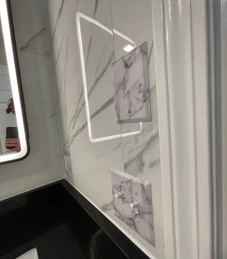 Custom camouflaged light switch and GFCI outlet covers designed to seamlessly match the grey marble wall tile.