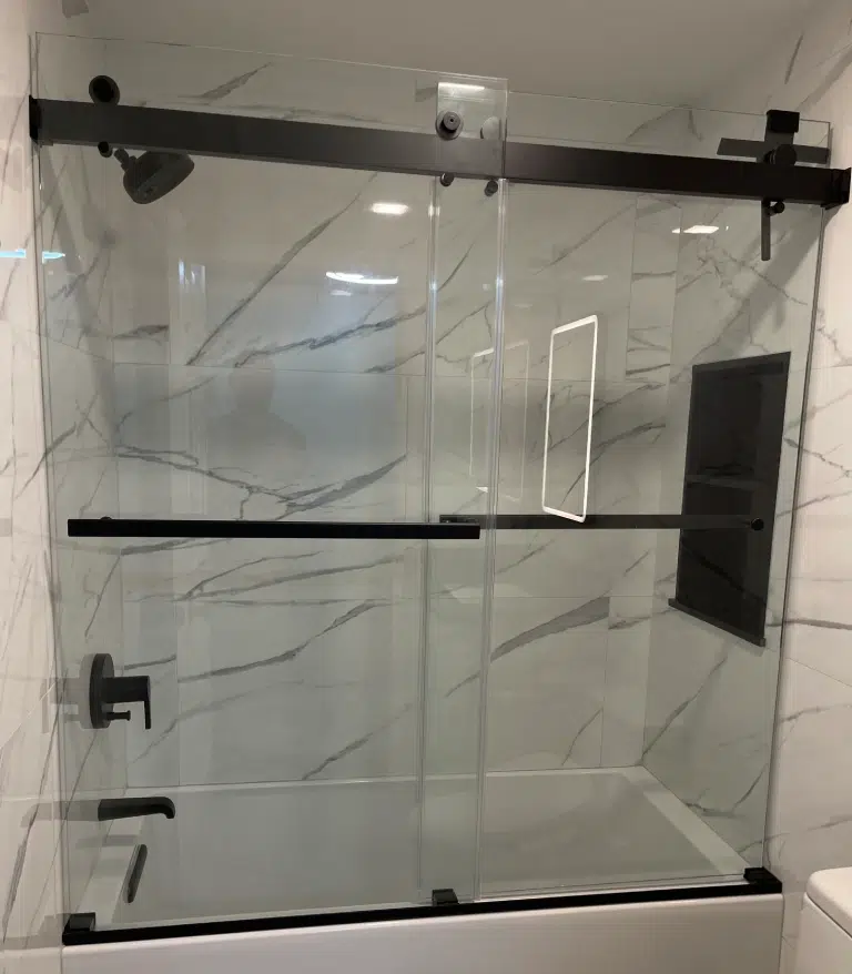 Custom sliding glass shower doors with heavy-duty matte black hardware installed over a new white soaking tub.