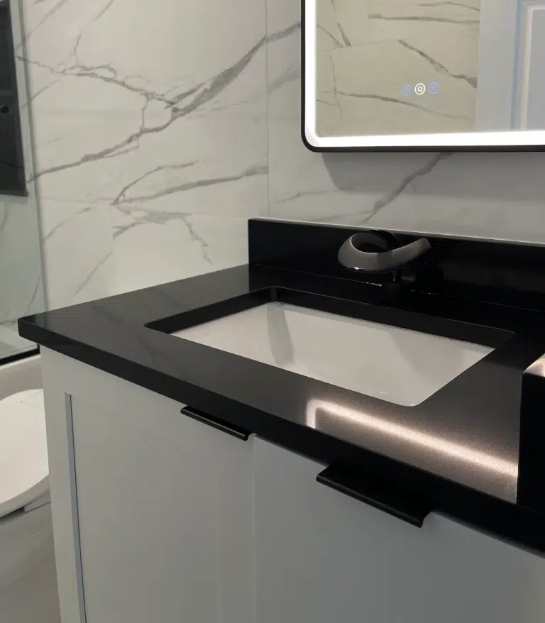 Matte black loop-spout faucet on a solid black vanity countertop in a high-contrast modern bathroom design.