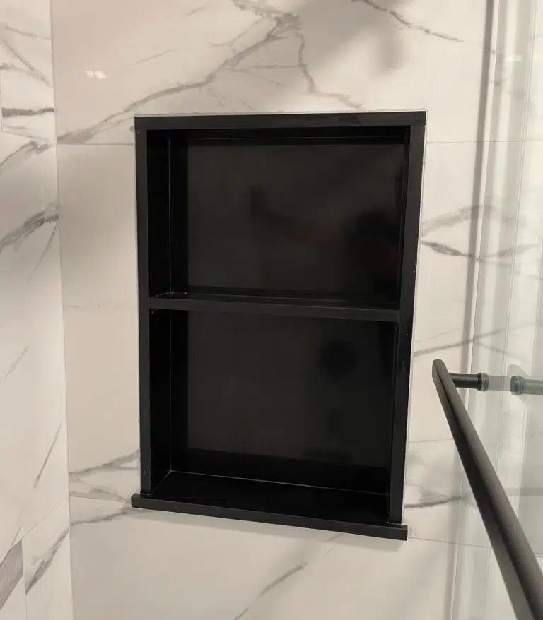 Custom recessed matte black double-shelf shower niche built into white marble-patterned porcelain wall tile.