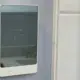 Smart tech bathroom addon showing a sleek white digital touchscreen thermostat controller mounted on a wall next to white tile.