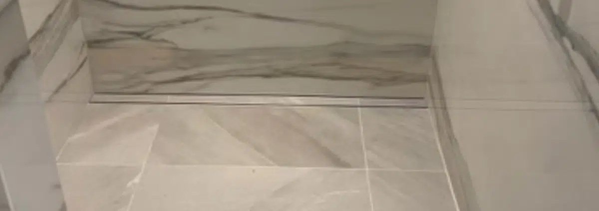 Modern bathroom remodel showing a luxury shower with marble-look slabs, a built-in floating bench, matte black fixtures, and a linear drain.