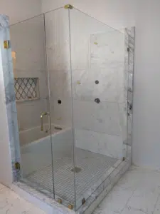 Custom glass shower enclosure featuring large-format marble porcelain tiles, elegant gold hardware, an accent tile niche, and an adjacent bathtub.