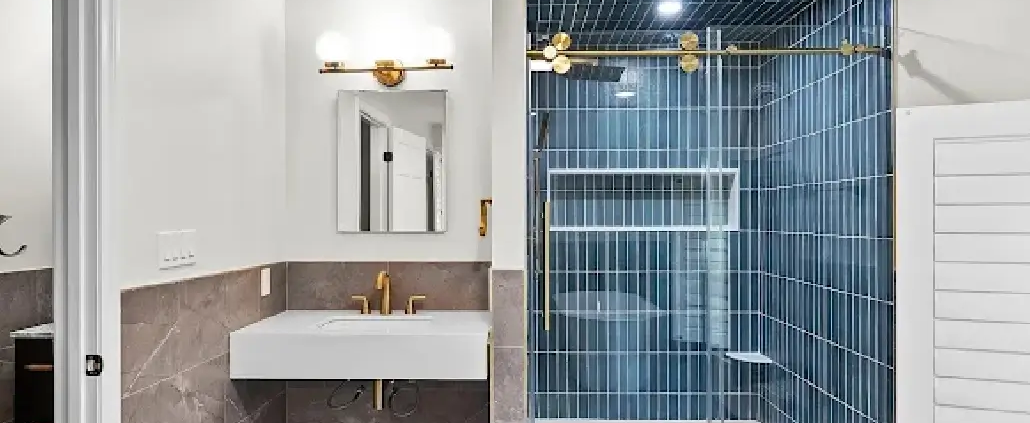 Small bathroom layout with a floating white sink, gold fixtures, gray tile wainscot and a navy vertical-tile walk-in shower, an idea for NH homes.