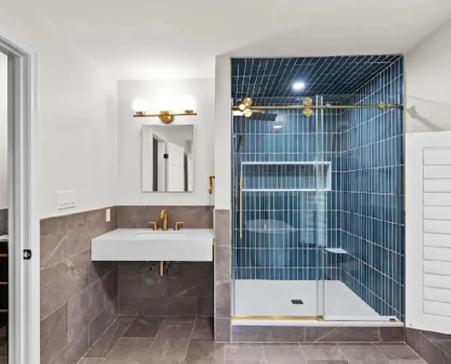 Small bathroom layout with a floating white sink, gold fixtures, gray tile wainscot and a navy vertical-tile walk-in shower, an idea for NH homes.